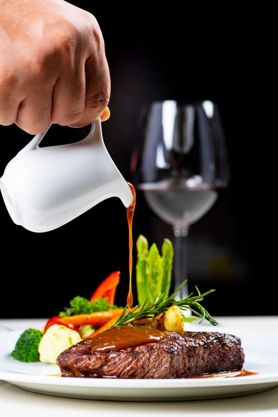 Salsa versata su una bistecca con verdure, con un calice di vino sullo sfondo.