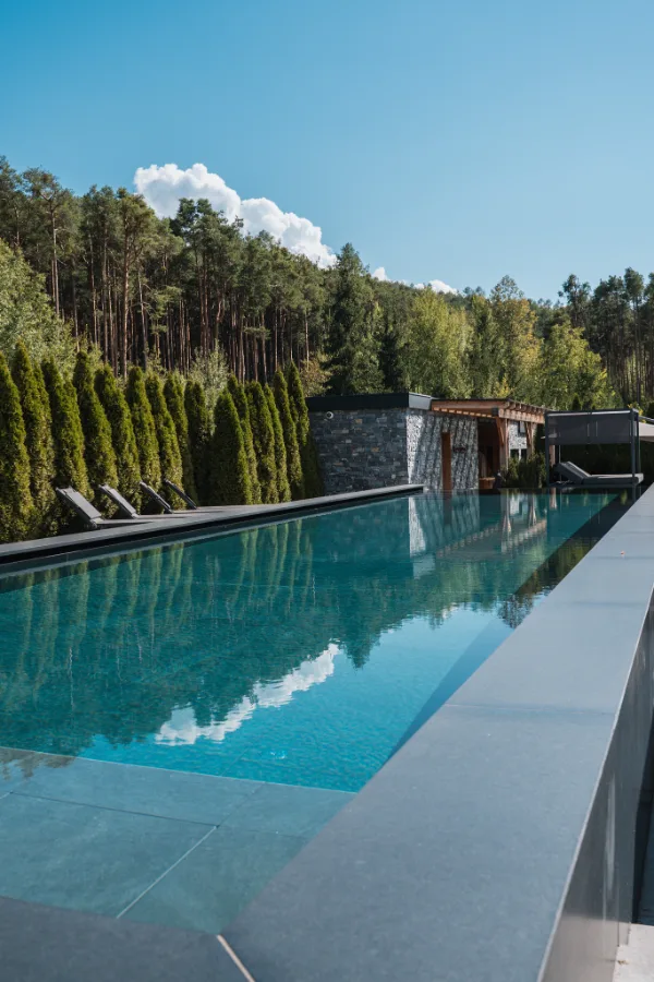 Piscina a sfioro di un hotel tra tuie e pini.