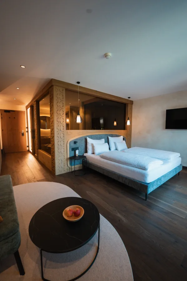Camera d'hotel con letto matrimoniale, legno chiaro e luci soffuse.